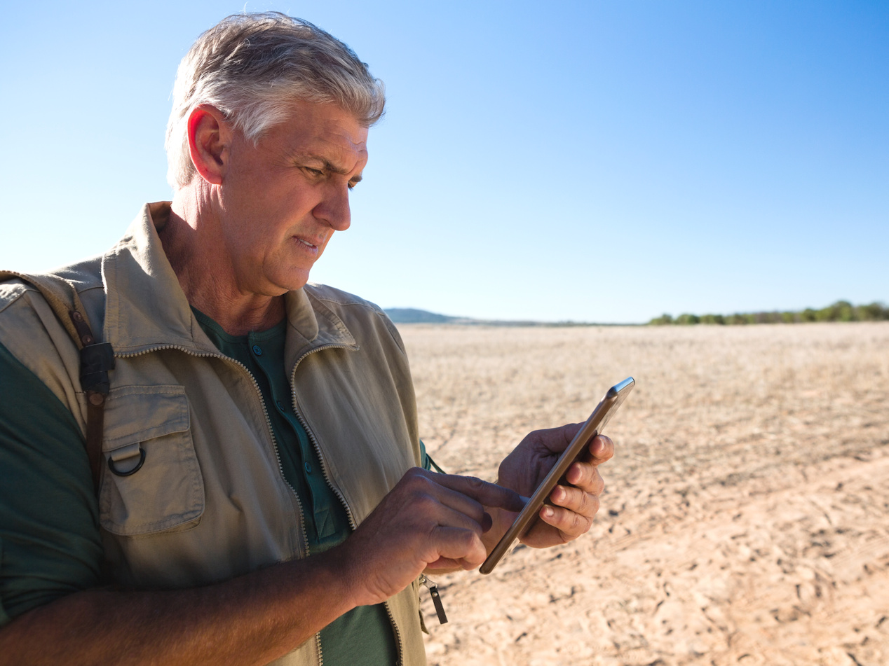 produtor segurando um tablet iPad na frente de terra arrada.